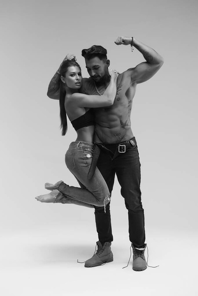 Black and white side view of topless woman and shirtless man looking at camera against gray background - Fotó, kép