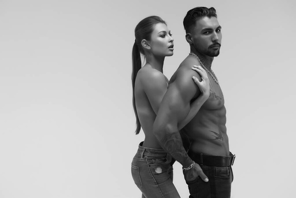 Hombre sin camisa tatuado blanco y negro y mujer en topless seductora mirando hacia otro lado - Foto, imagen