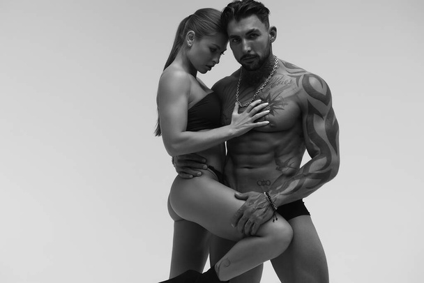 Hombre sin camisa tatuado blanco y negro y mujer en topless seductora mirando hacia otro lado - Foto, Imagen
