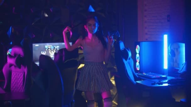 Młoda, seksowna kobieta z kucykiem trzymająca joysticka w klubie gier neonowych i dmuchająca gumę do żucia - Materiał filmowy, wideo
