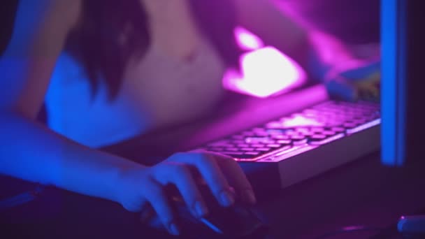 Mujer joven en gafas jugando juegos en línea en el club de juegos de neón - ratón y teclado iluminado - Imágenes, Vídeo