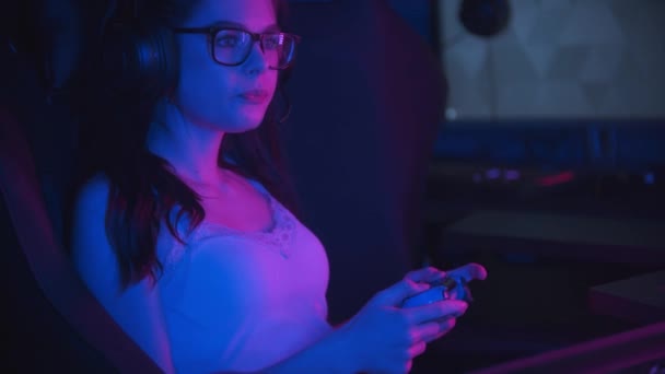 Giovane bella donna in occhiali giocare giochi online nel moderno club di gioco al neon e masticare una gomma da masticare - Filmati, video