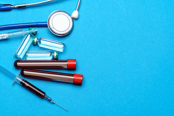 Stethoscope, syringe, test tubes with blood samles and ampoules with medicine or vaccine over blue background - Photo, Image