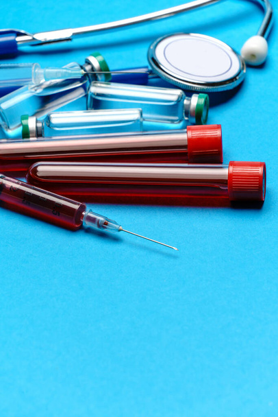 Stethoscope, syringe, test tubes with blood samles and ampoules with medicine or vaccine over blue background - Fotoğraf, Görsel