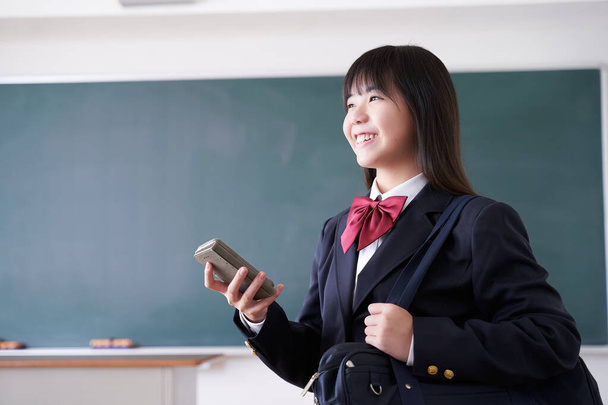 Eine japanische Realschülerin lächelt, als sie ihr Telefon im Klassenzimmer bedient - Foto, Bild