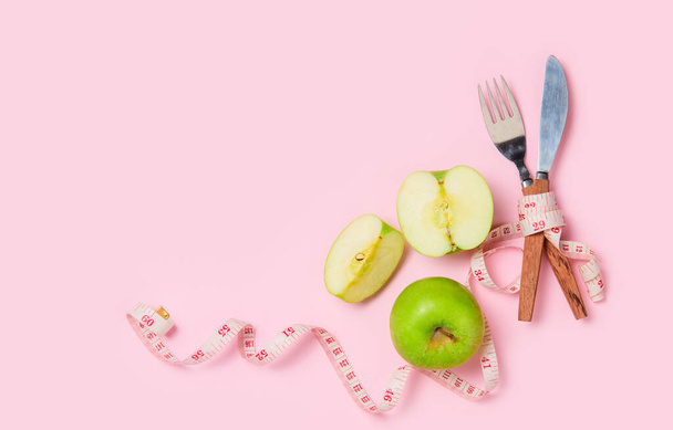 Zöld alma mérőszalag körül villa és kés elszigetelt rózsaszín alapon, koncepció a cél, hogy lefogy, a cél a diéta - Fotó, kép