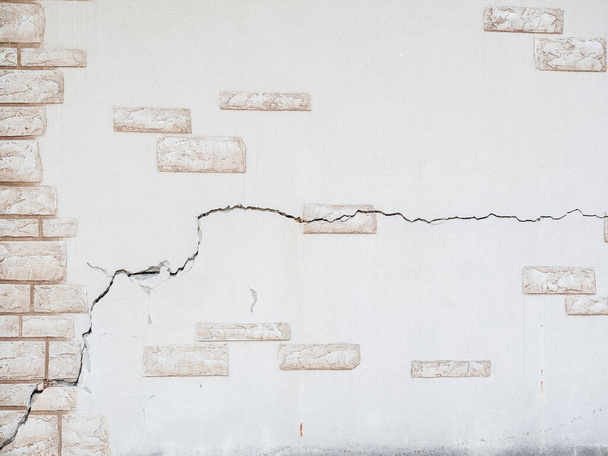 Una pared con yeso decorativo en forma de mampostería con una gran grieta. Textura de fondo. Pantalla completa - Foto, imagen