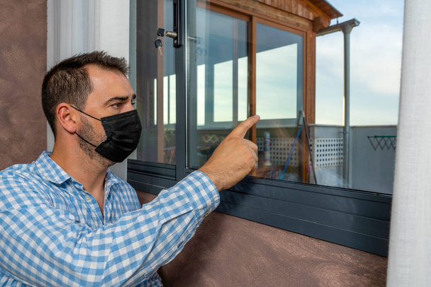 Hombre enfermo de coronavirus mirando por la ventana y usando máscara para la protección y la recuperación de la enfermedad en casa. Concepto de desolación - Foto, Imagen