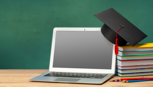 Онлайн-образование. Дистанционное обучение дома. Ноутбук и стопка книг в шляпе выпускника - Фото, изображение
