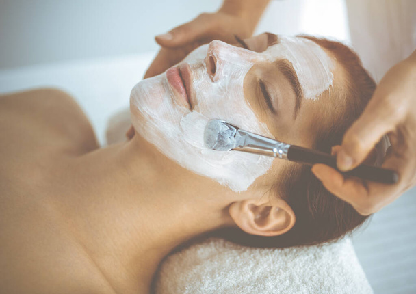 Beautiful brunette woman enjoying applying cosmetic mask with closed eyes. Relaxing treatment in medicine and spa concepts - Φωτογραφία, εικόνα