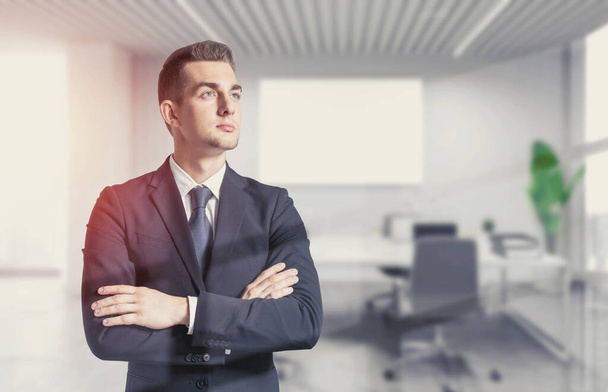 Portrait of confident young businessman standing with crossed arms in blurry CEO office. Concept of leadership. Toned image - Фото, изображение