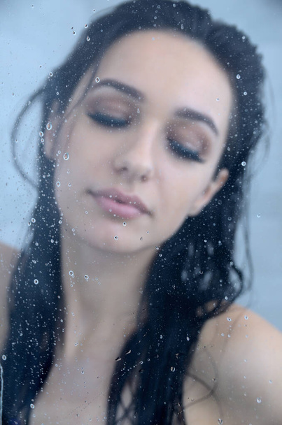 Junge Frau mit nassen Haaren unter der Dusche, sichtbare Wassertropfen. Konzentriere dich auf Glas mit Wassertropfen. Schöne Brünette, Miss Niederschlesien posiert zu Hause, Indoor-Fotosession.  - Foto, Bild