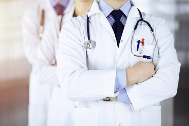 Group of modern doctors standing as a team with crossed arms and stethoscopes in a sunny hospital office. Physicians ready to examine and help patients. Medical help, insurance in health care, best - Photo, Image