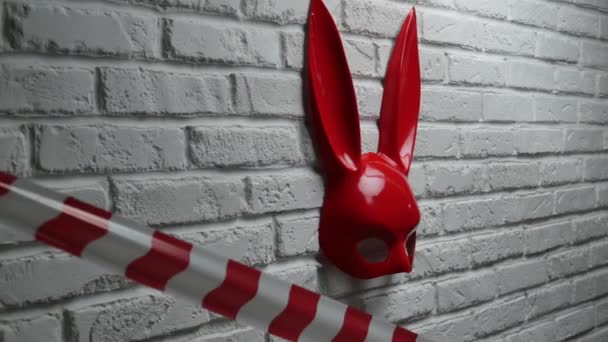 czerwona maska królicza na ścianie z białej cegły oraz czerwono-biała taśma sygnałowa - Materiał filmowy, wideo