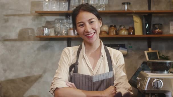 Портрет молодой азиатки-баристы, улыбающейся в городском кафе. Владелец малого бизнеса индонезийская девушка в фартуке расслабляет зубастую улыбку, глядя в камеру, стоящую у стойки в кафе. - Кадры, видео