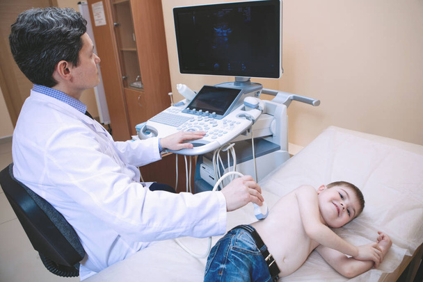 Examen ecográfico del niño. El médico hace un escáner abdominal de un niño en una clínica médica. - Foto, imagen
