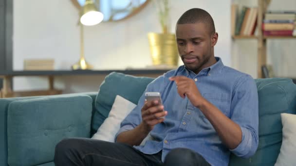 Serious Young African Man using Smartphone on Sofa  - Video, Çekim