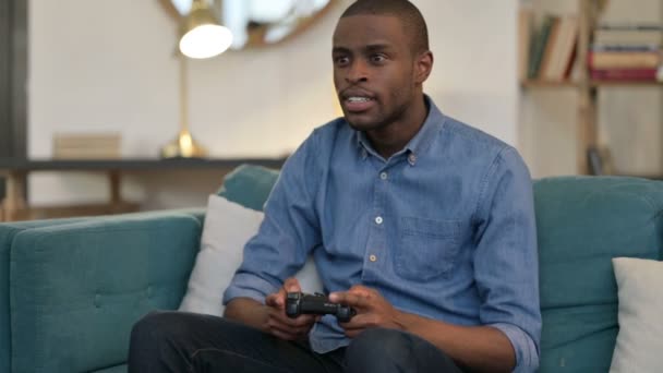 Молодой африканский человек играет в видеоигры на диване - Кадры, видео