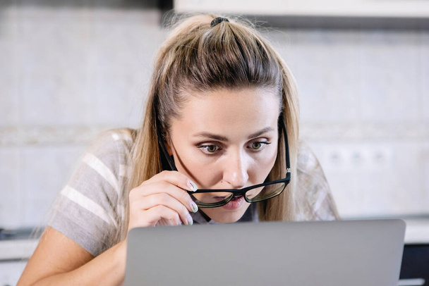 Woman looks in surprise through glasses at the laptop monitor. - Φωτογραφία, εικόνα