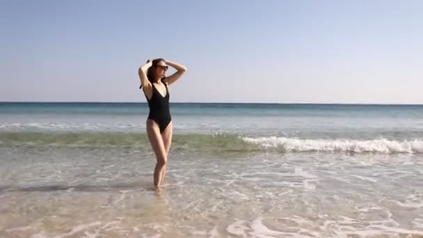 hermosa chica en la playa en un traje de baño junto al mar. chica bronceada en gafas de sol. estado de ánimo marino - Metraje, vídeo