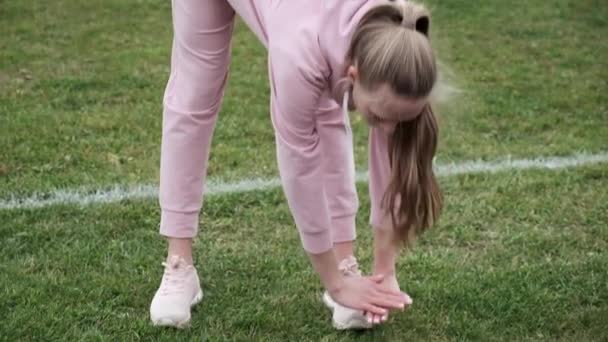 fiatal nő sportruházatban nyújtózkodó test sportstadionban focipálya - Felvétel, videó