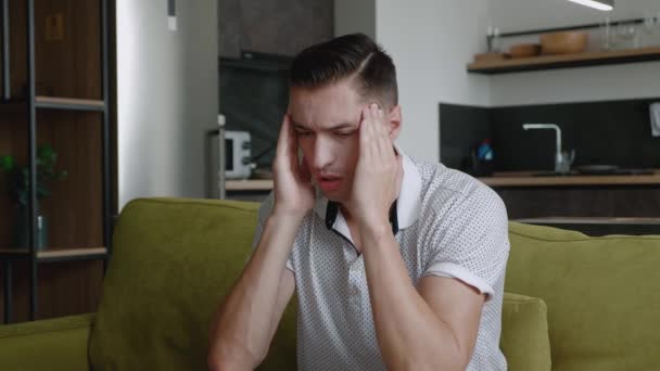 Nezdravý mladý muž trpí silnou bolestí hlavy, zatímco sedí doma na pohovce. Zoufalý muž v depresi se obával problémů. Psychické problémy. - Záběry, video