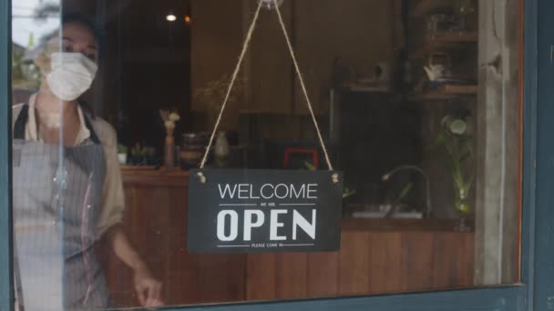Young Asia girl wear face mask turning a sign from open to closed sign on glass door cafe after coronavirus lockdown quarantine. Owner small business, food and drink, business financial crisis concept - Footage, Video