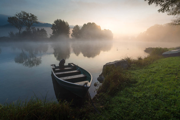 Calm scenic picture of small fishing boat on the Adda river on a hazy sunrise with foliage - Foto, Imagem