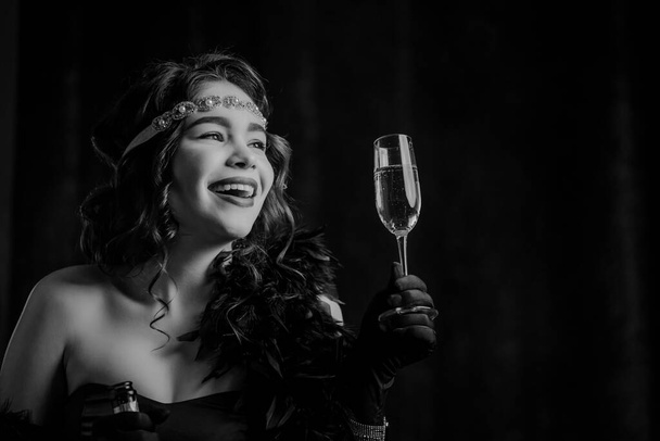 Vintage Art Deco styled woman dressed raises glass of champagne like toast, drinking wine on velours background. Roaring twenties, retro, party, fashion concept - Photo, Image