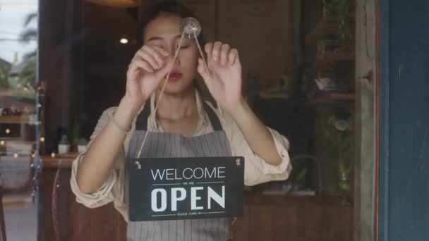 Mladá asijská manažerka po karanténě koronaviru otočila ceduli z otevřené na zavřenou na skleněnou kavárnu. Vlastník malé firmy, jídlo a pití, obchodní finanční krize koncept. - Záběry, video