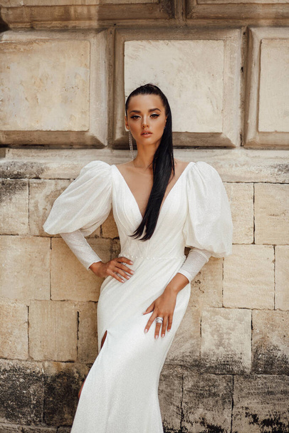 fashion outdoor photo of beautiful woman with dark hair in luxurious wedding dress and accessories posing in the summer street - Foto, afbeelding