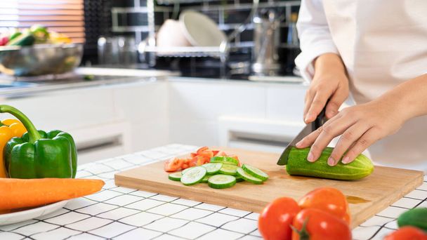 young Asian woman is preparing healthy food vegetable salad by Cutting cucumber for ingredients on cutting board on light kitchen, Cooking At Home and healthy food concept - Foto, Bild