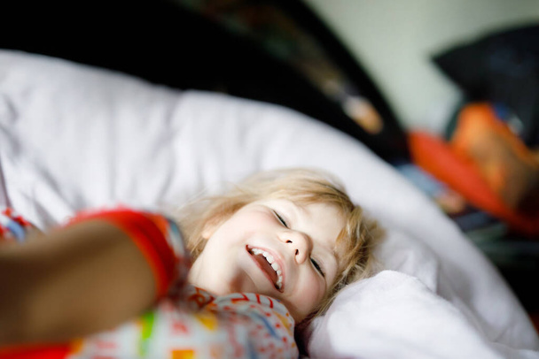 Ένα κοριτσάκι που περνάει καλά στο κρεβάτι μετά το ξύπνημα. Υγιές παιδί άλμα και να παίξετε κρυφτό με τους γονείς. Αξιολάτρευτο παιδί στο σπίτι, οικογενειακή ζωή. - Φωτογραφία, εικόνα