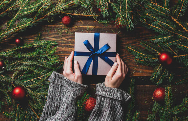 Female hands hold gift box next to Christmas decoration on a table  - Photo, Image