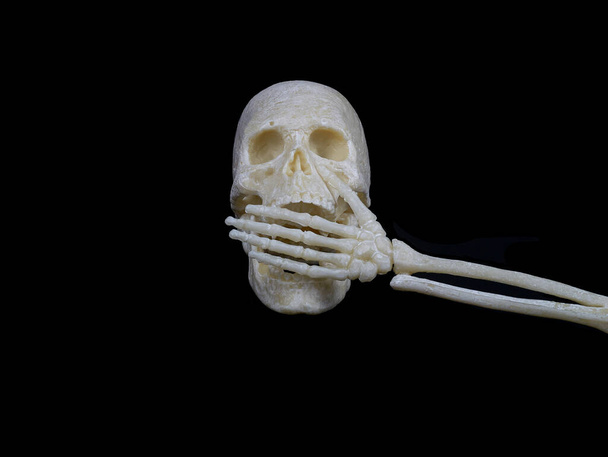 Human skull covers its mouth with a skeleton hand, cannot speak, sign of silence or violence - Fotoğraf, Görsel