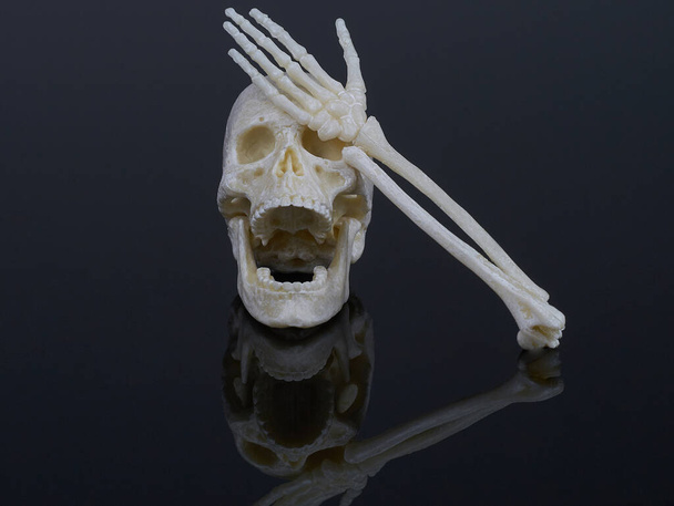 een menselijke schedel met een open mond die lijkt op lachen bedekt zijn ogen met een skelet hand, hand gezicht - Foto, afbeelding