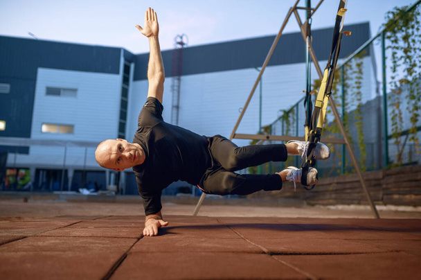 Sportive man doing balance exercise with ropes on sports ground outdoors. Slim female person in sportswear, outside fitness training, fit workout - Photo, Image