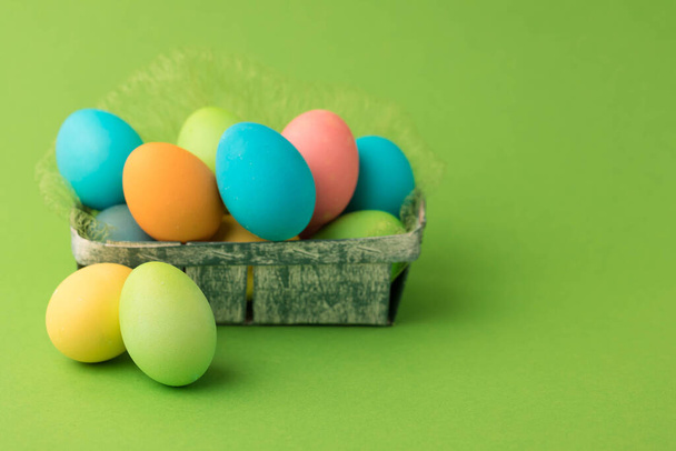 Painted Easter eggs in a wicker wooden basket on a green background. - Foto, Imagen