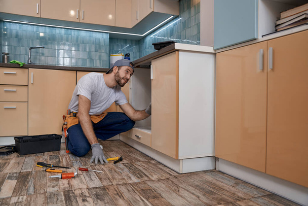 Молодой кавказский ремонтник устанавливает кухонную мебель - Фото, изображение