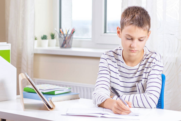 Dijital tablet bilgisayarda yazan çocuk, beyaz masada ödev yapıyor. Çevrimiçi öğrenim, uzaktan eğitim, evde uzaklık dersleri - Fotoğraf, Görsel