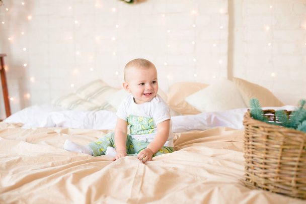 Little boy  in pajama have fun in in a Scandinavian style bedroom decorated with Christmas garlands and needles on a large bright bed. Christmas mood. Christmas mood. Family time - Zdjęcie, obraz