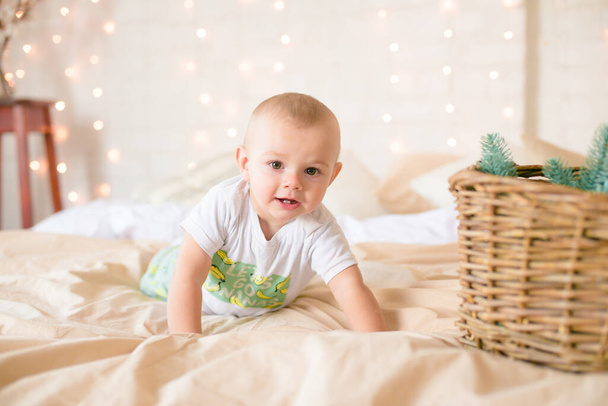 Little boy  in pajama have fun in in a Scandinavian style bedroom decorated with Christmas garlands and needles on a large bright bed. Christmas mood. Christmas mood. Family time - 写真・画像