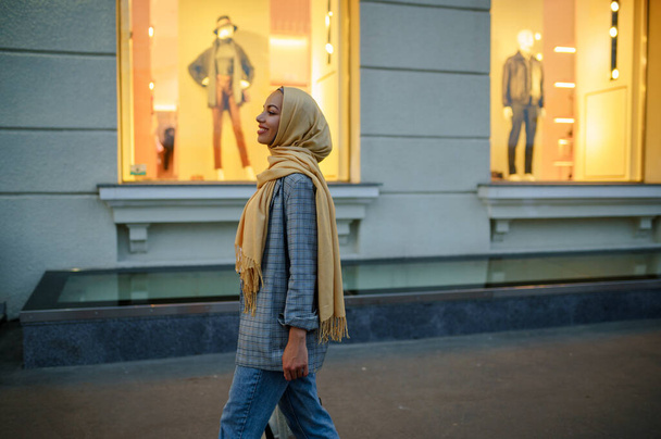 Arab girl in hijab looking on showcase of fashion store in downtown. Muslim woman walking on street. Female student in big city - Foto, immagini