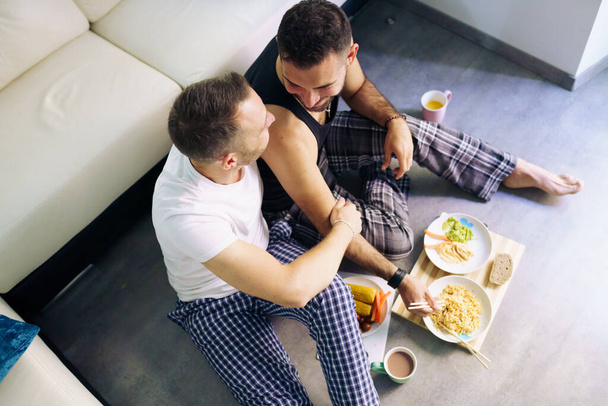 Homosexuell pärchen essen zusammen sitzen auf ihre wohnzimmer boden. - Foto, Bild