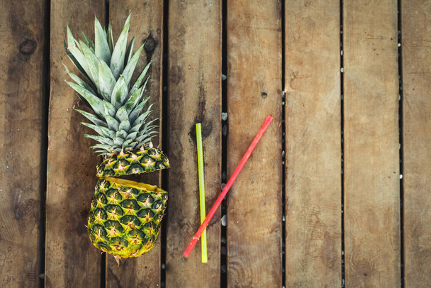 Накладные кадры коктейля из свежих фруктов ананаса с палкой на деревенском деревянном фоне. Концепция тропических летних каникул. Солнечный день на пляже тропического острова - Фото, изображение