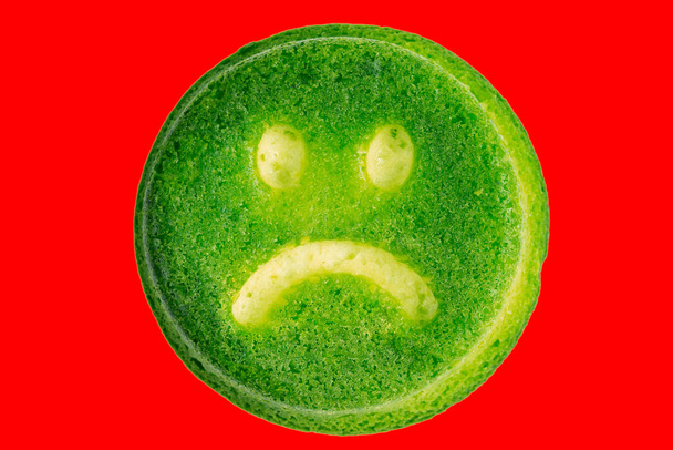 unglückliches grünes Gesicht Kekskeks isoliert auf rotem Hintergrund in flacher Laien-Perspektive. - Foto, Bild