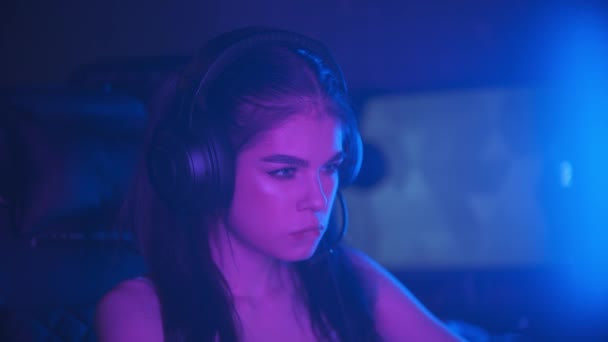 Młoda atrakcyjna kobieta siedzi w neonowym klubie gier i gra w gry - gryzie wargę - Materiał filmowy, wideo