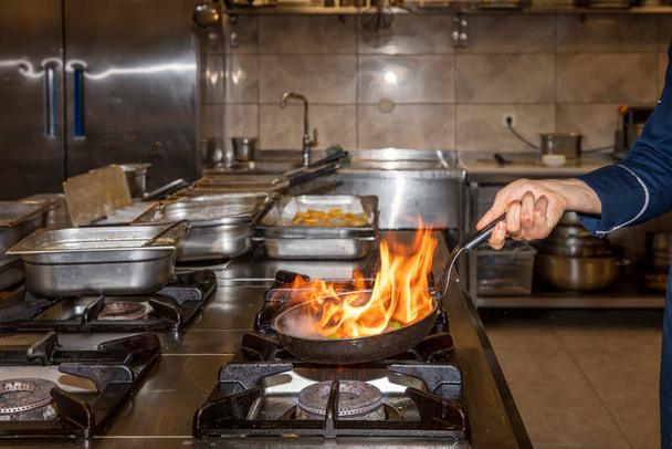 Láng a serpenyőben. Professzionális séf teszi flambe élelmiszer az étterem konyhájában. Szakács főzés nyitott tűz serpenyőben a tűzhelyen.  - Fotó, kép