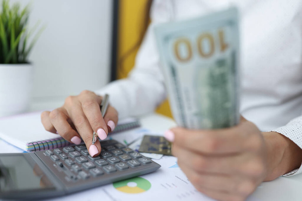 Female hands are holding one hundred dollar bills and working on calculator. - 写真・画像
