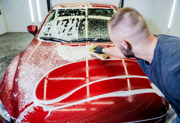 Εργαζόμενος πλύσιμο κόκκινο αυτοκίνητο με σφουγγάρι σε πλυντήριο αυτοκινήτων - Φωτογραφία, εικόνα